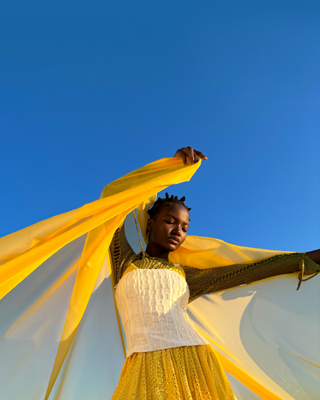 Portrait d’une personne tenant un foulard jaune transparent, regardant vers le bas et prenant la pose en plein soleil
