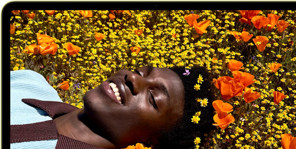 MacBook Neo, couleur jaune agrume, écran affichant une personne souriante allongée dans un champ de fleurs ensoleillé