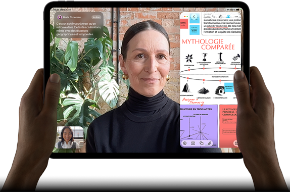 iPad Pro, face avant, orientation paysage, noir sidéral, angles arrondis, cadre noir de l’écran, mains tenant les côtés gauche et droit, écran affichant une conversation FaceTime en cours de traduction en direct, et une app éducative montrant une présentation de la mythologie comparée avec du texte, des diagrammes et des notes manuscrites