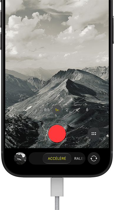 iPhone 18 Pro, face avant, affichant un paysage montagneux, avec le mode caméra incrusté en mode Accéléré, avec câble d’alimentation branché sur le port de charge
