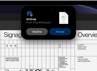 L’écran affiche la Dynamic Island avec une demande AirDrop dans une petite fenêtre au-dessus d’un fichier Adobe Acrobat ouvert